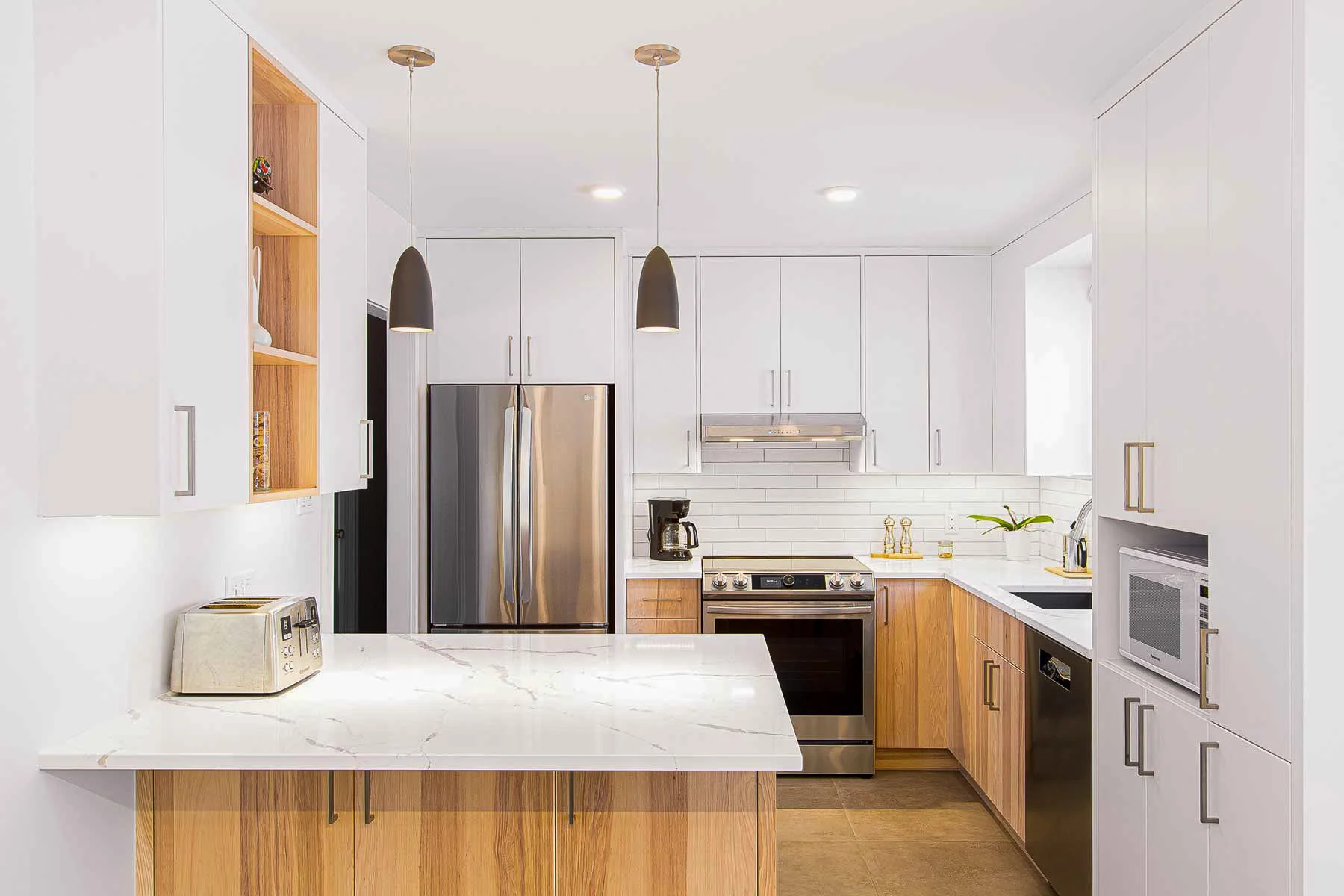 Cuisine moderne avec armoires blanches, plan de travail en marbre, réfrigérateur, four, micro-ondes, cafetière, et décor minimaliste.