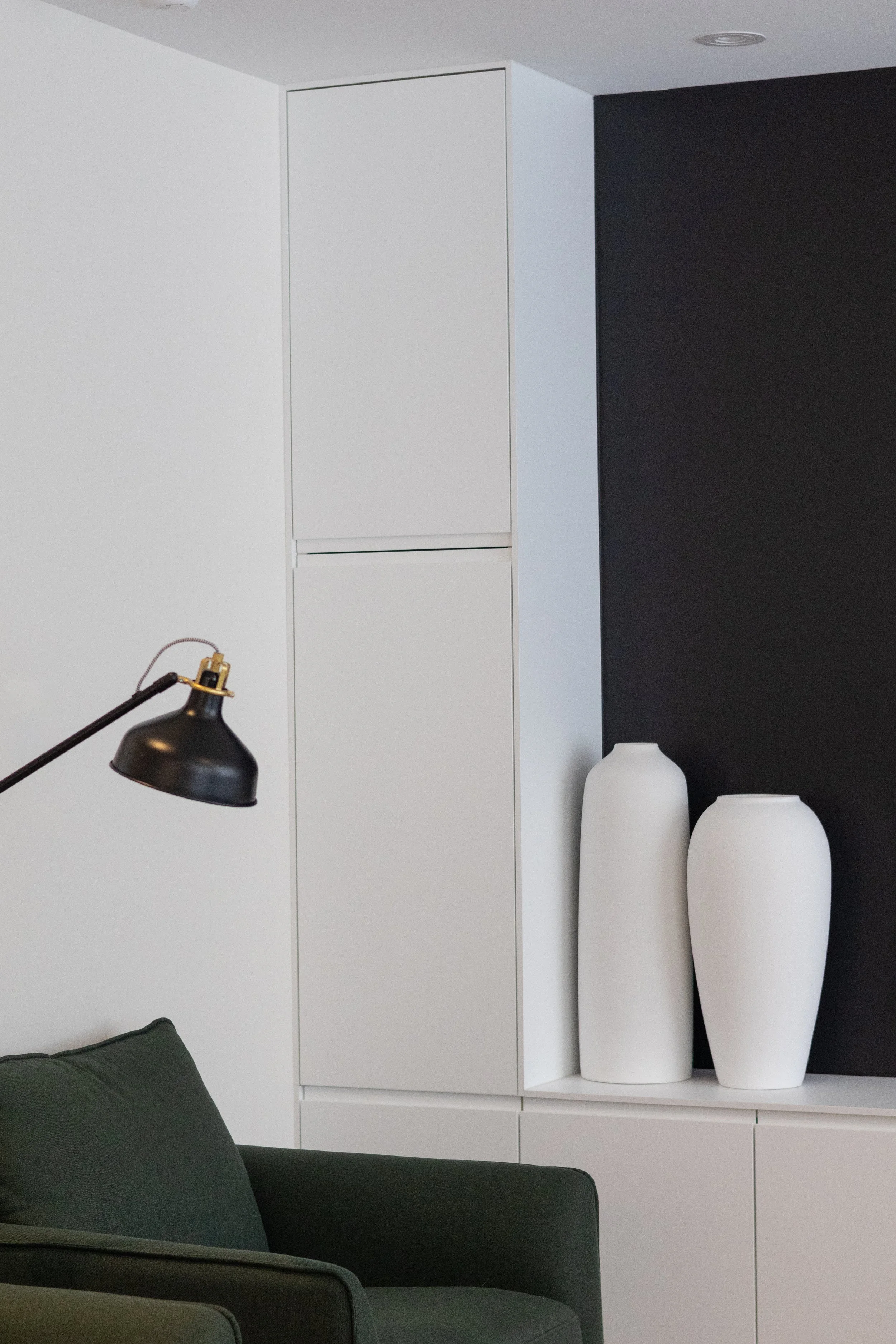 Intérieur moderne avec un mur noir, deux grands vases blancs et un canapé vert foncé.