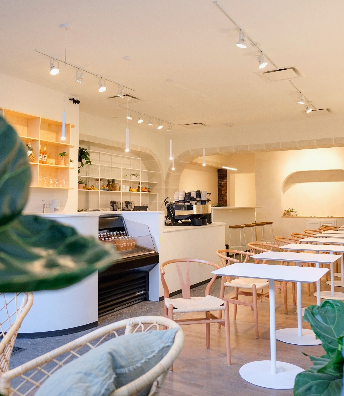 Intérieur d'un café moderne avec tables blanches, chaises en bois clair, décor minimaliste et chaleureux agrémenté d'arches.