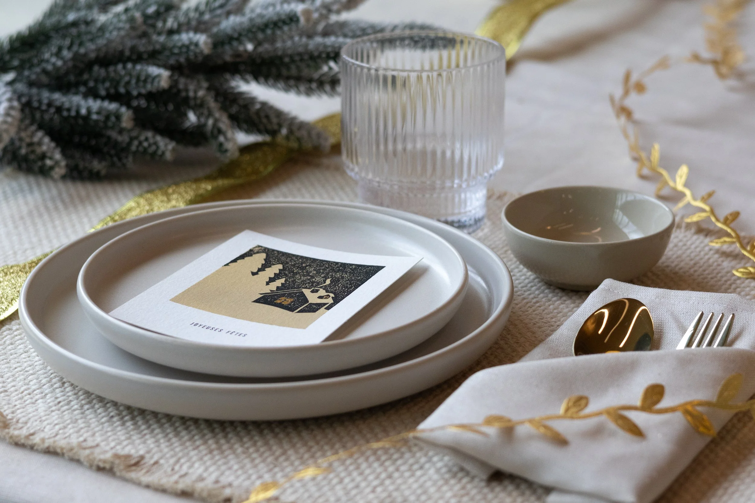 Table de fête décorée avec du sapin, une guirlande de feuilles dorées et une carte de voeux représentant un paysage de montagnes enneigées.