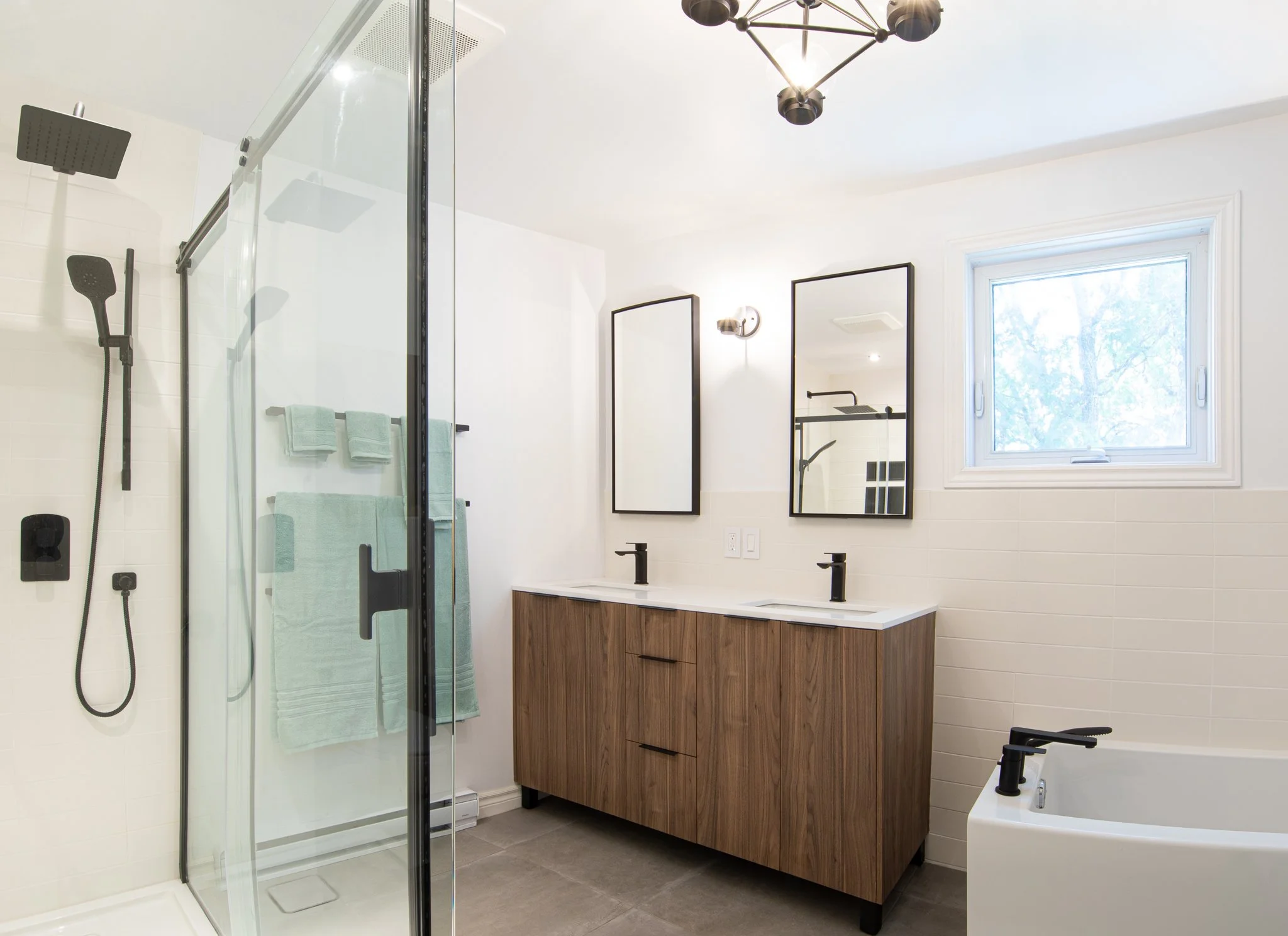 Salle de bain moderne avec douche vitrée, double lavabo avec meuble en bois, baignoire, miroir, fenêtre, et éclairage