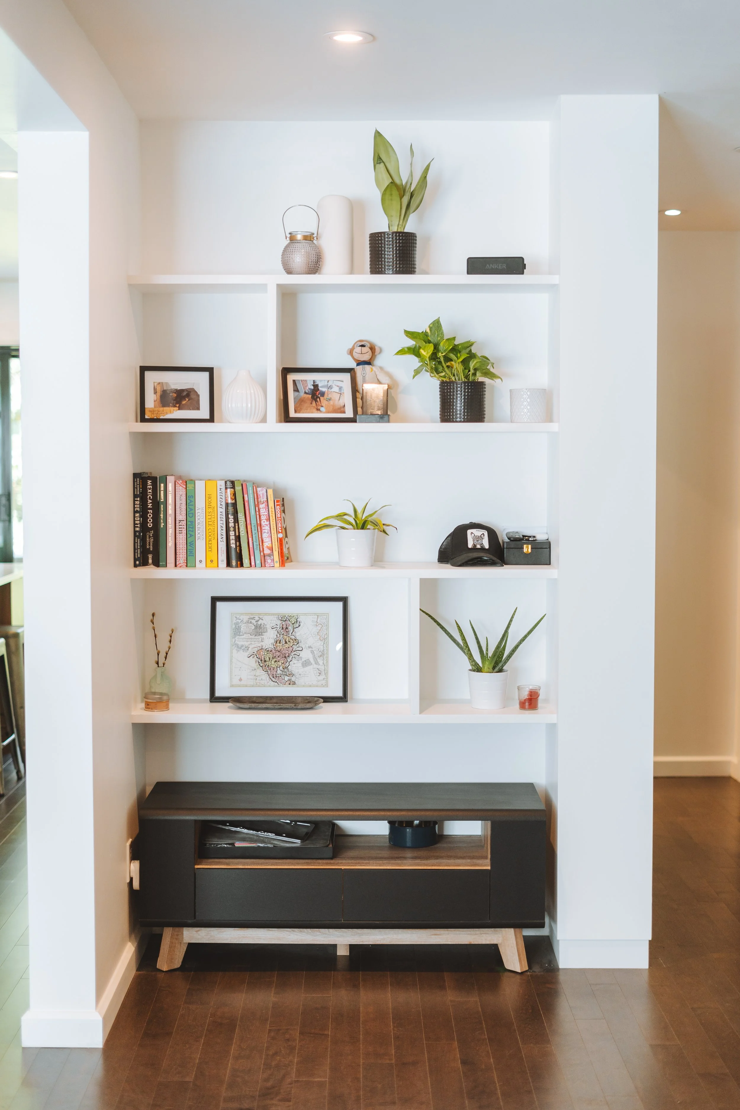 Étagère blanche décorée de plantes en pot, livres, cadres photo, objets décoratifs et un téléphone à l'intérieur d'une maison.