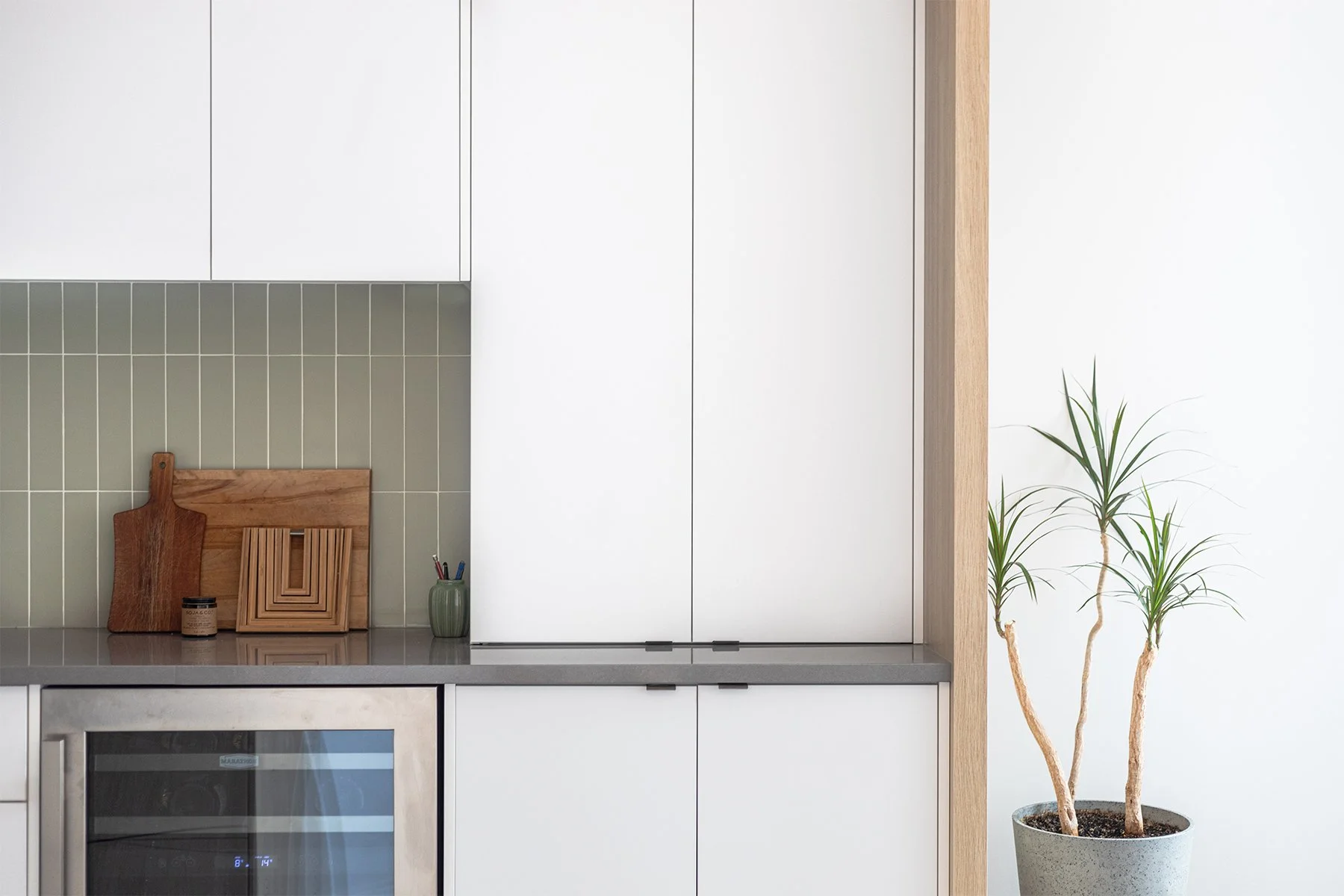 Cuisine moderne avec des cabinets blancs, une touche de bois, un comptoir de quartz gris et un dosseret en céramique vert sauge.