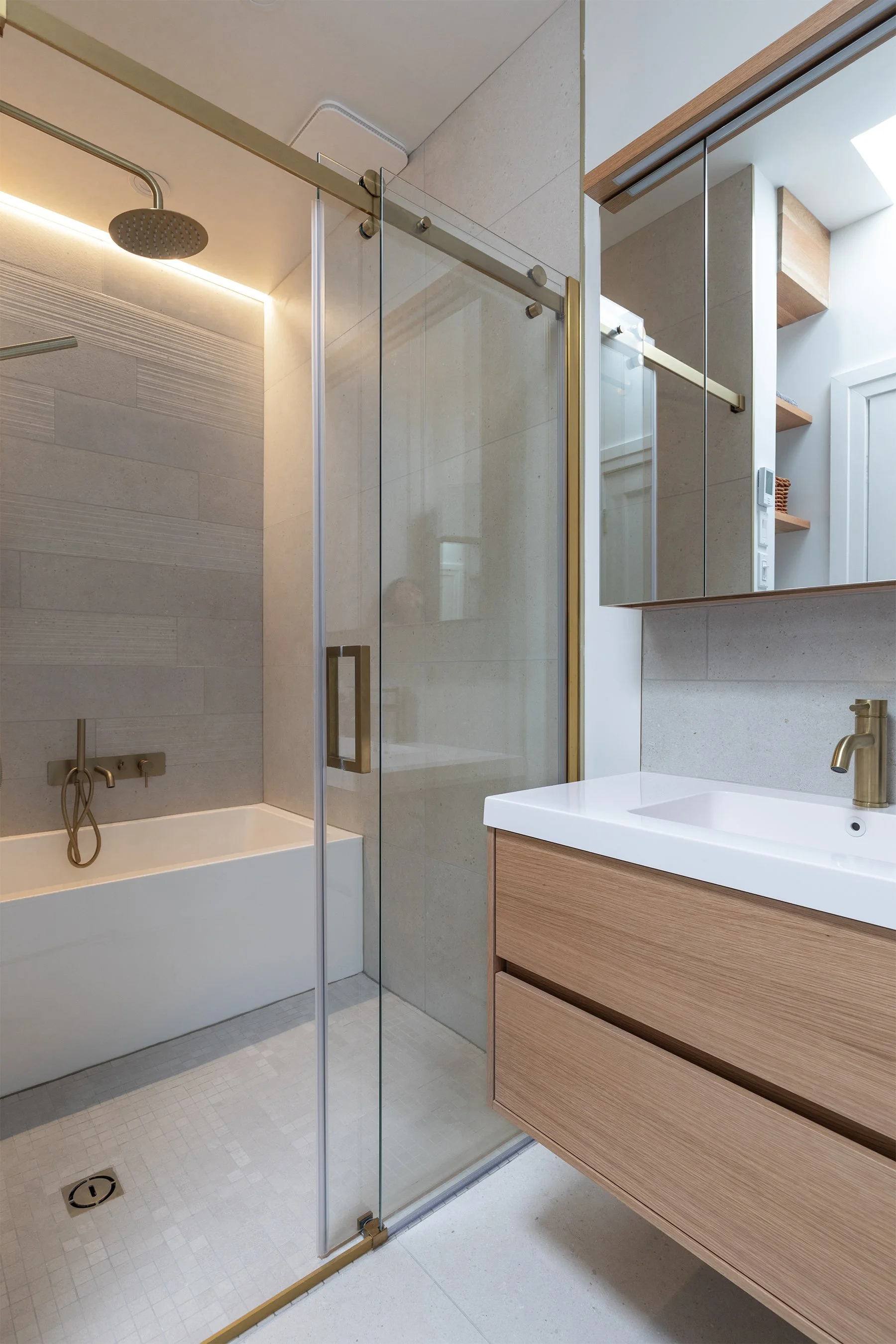 Salle de bain moderne avec douche en verre, baignoire, lavabo en bois avec robinetterie en or. Étagères en bois et miroir au mur.