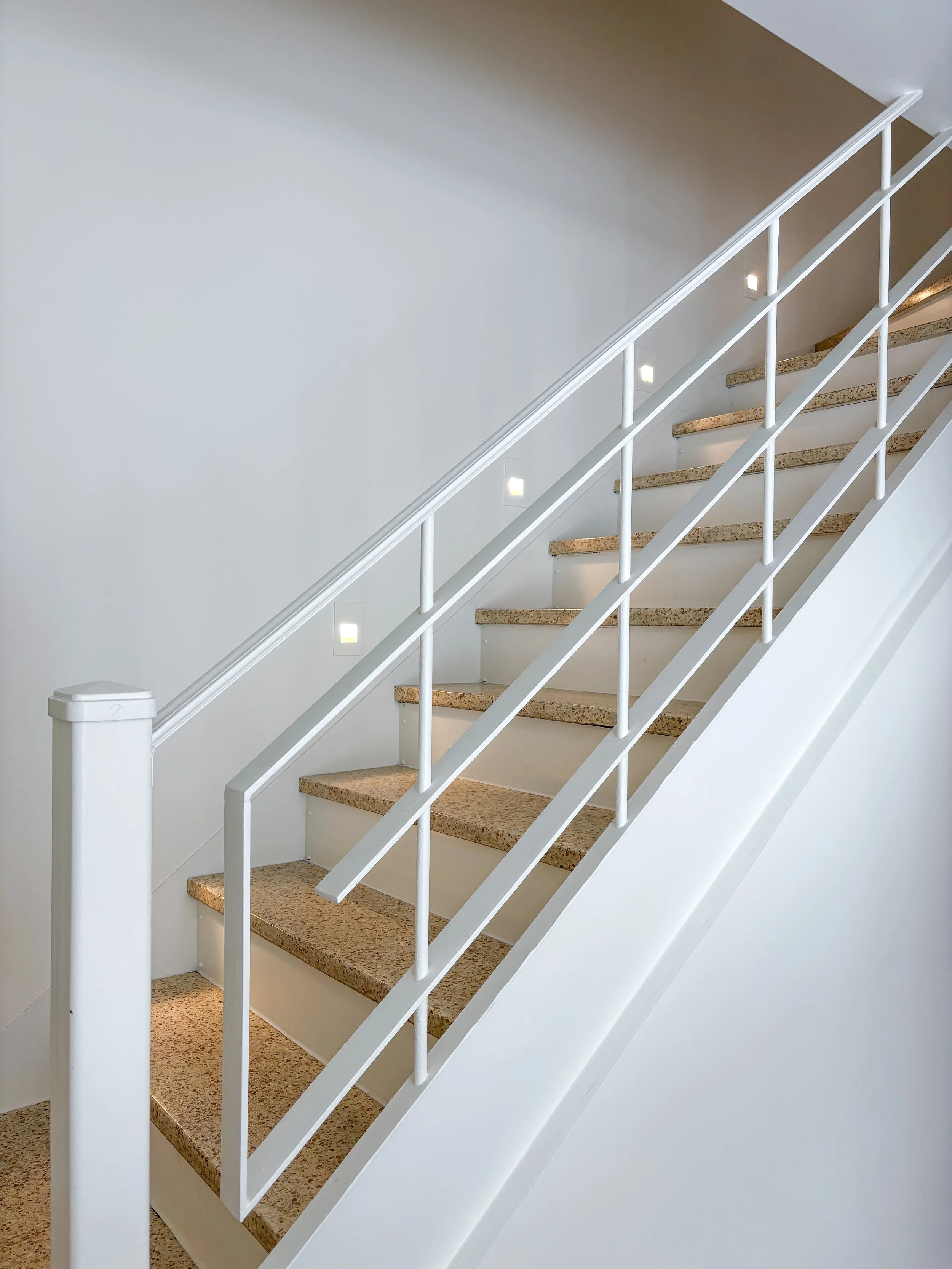 Escalier intérieur avec marches en marbre beige, rampe blanche et éclairage intégré dans le mur.
