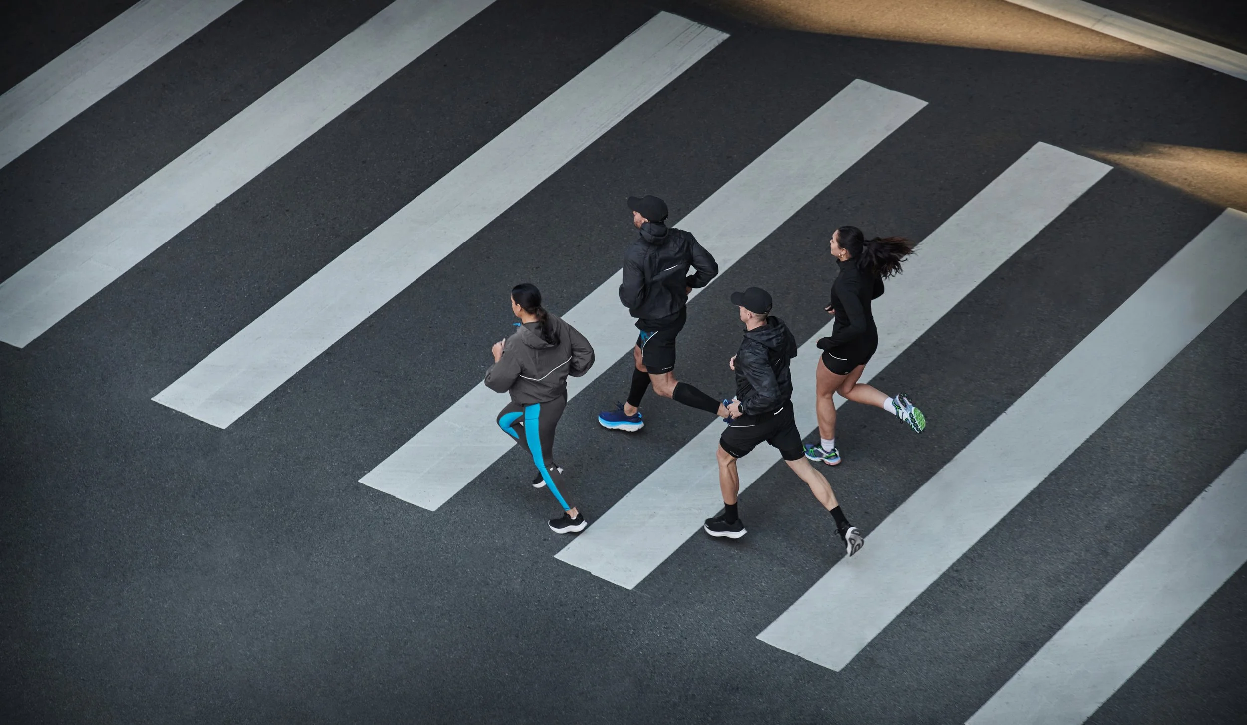 Four people walking across a crosswalk in athletic clothing on a dark road.