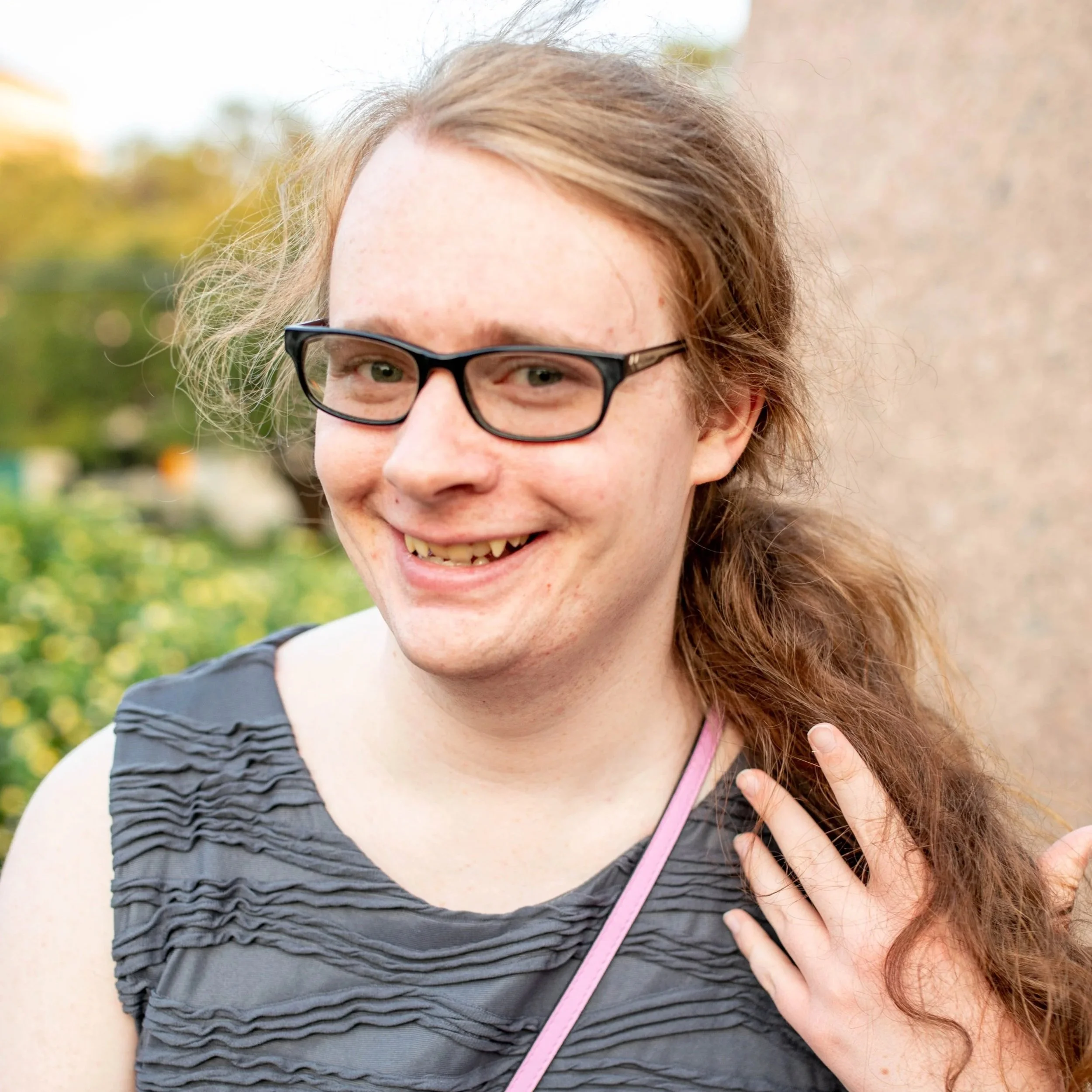 Melody, a white agender brunette, smiles and plays with hir hair
