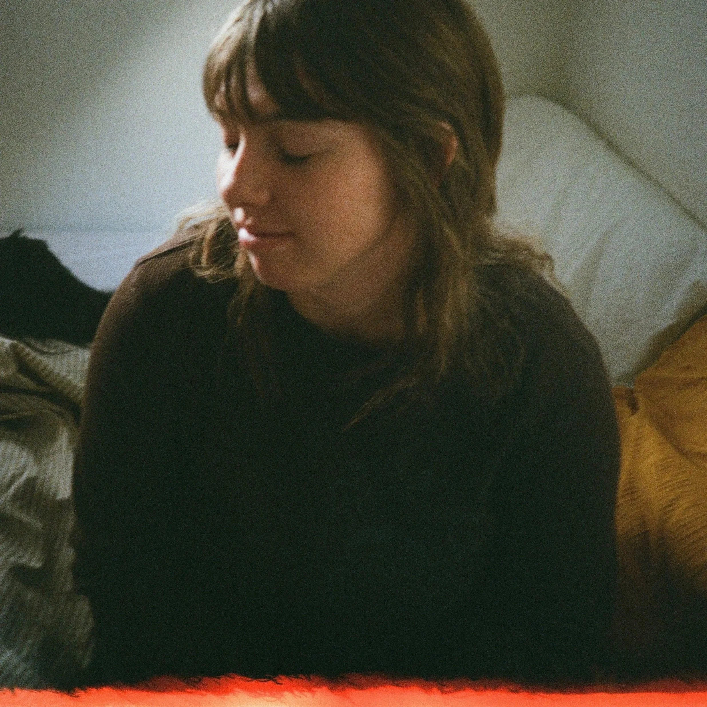 Jordan is a white female with medium brown hair. Jordan is wearing a brown long sleeve shirt and is facing away from the camera with a slight smile and her eyes closed. This picture was taken in film.
