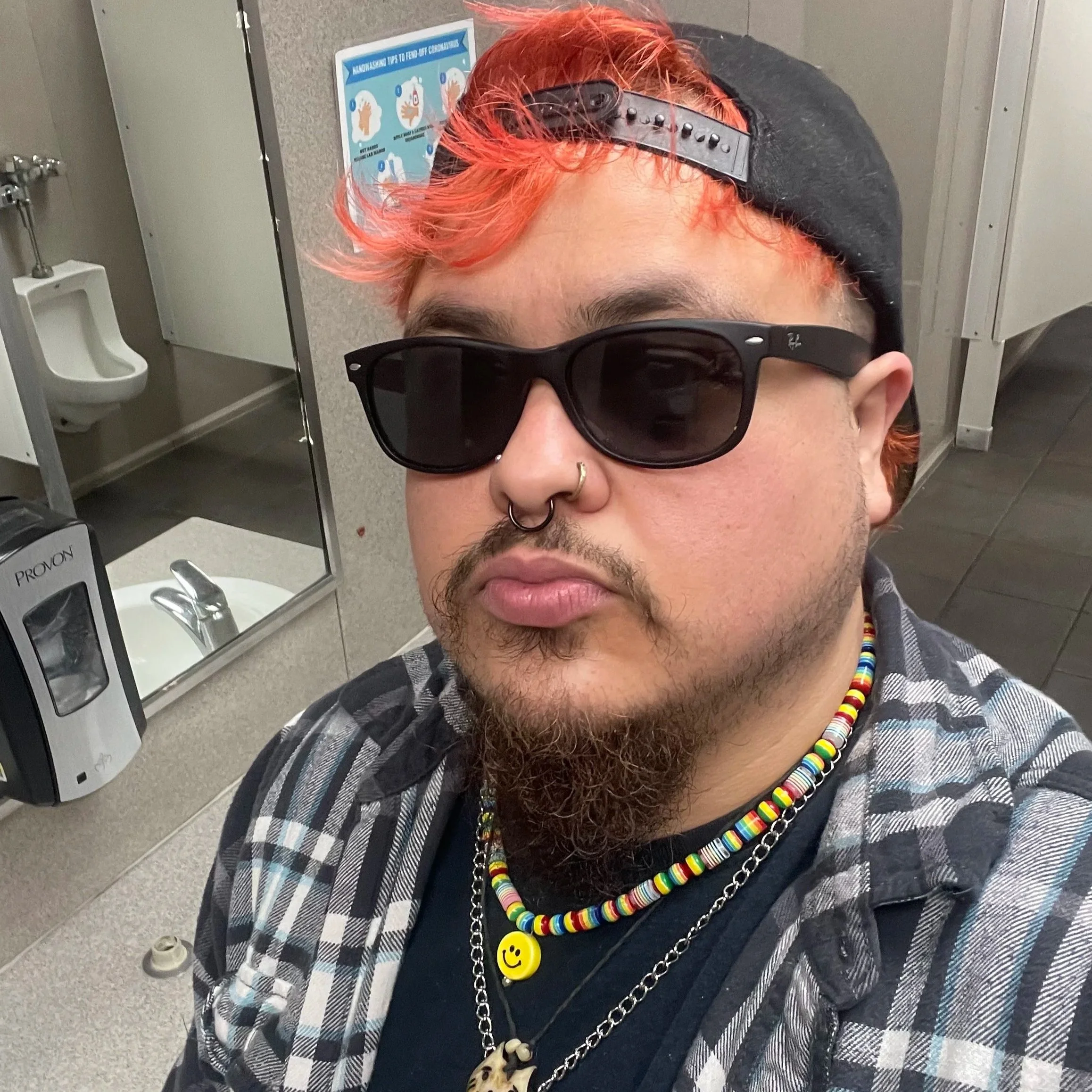Nick is a light brown Latine baddie with a blood orange Mohawk and a backwards baseball cap, Black sunglasses, a black shirt and black blue and yt flannel. They have necklaces, rainbow smiley face, koi fish and a green necklace that reads “faggot”