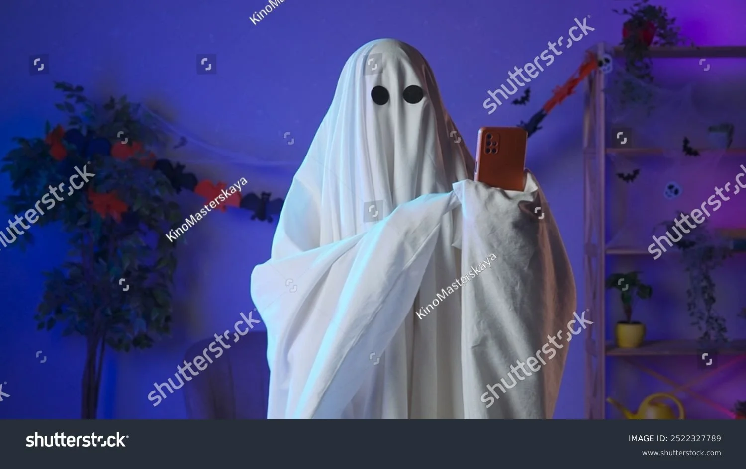 stock-photo-funny-halloween-ghost-in-white-sheet-with-black-eyes-in-dark-room-talking-on-smartphone-by-video-2522327789.jpg