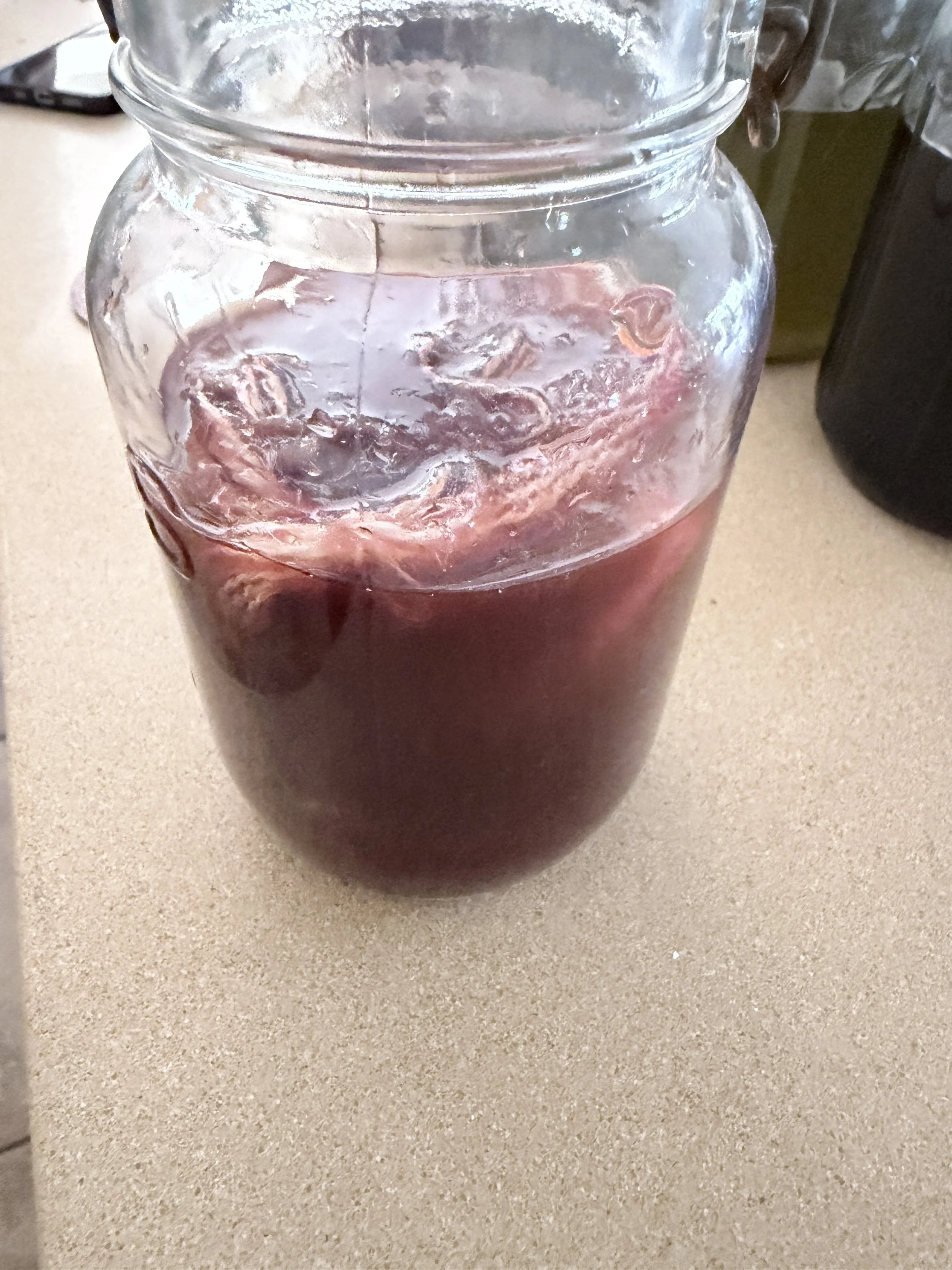 Glass jar of madder root dye, a cloudy, dark red liquid.