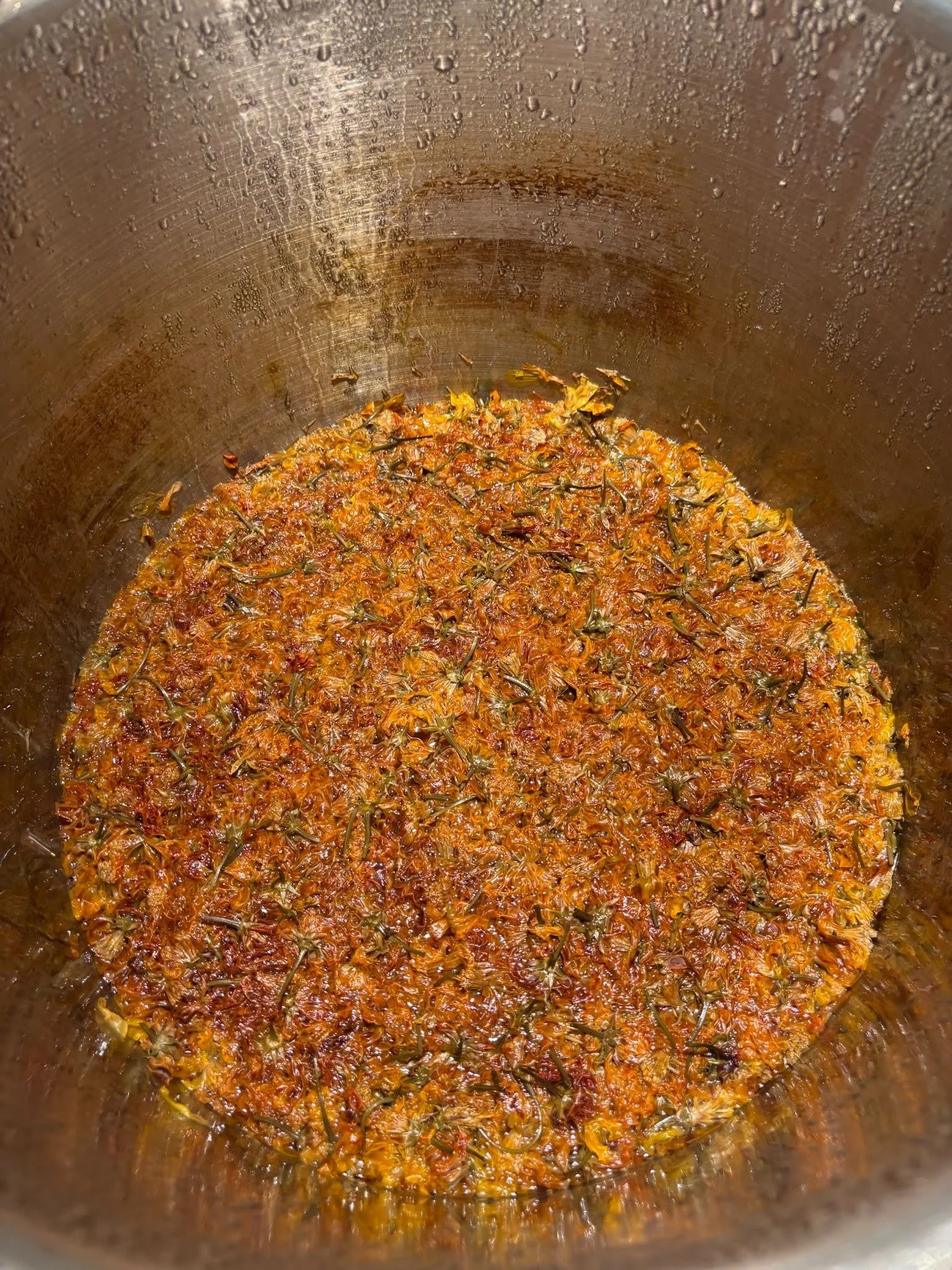 Yellow-orange coreopsis flowers simmering in water at the bottom of a large pot.