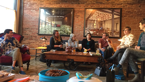A book club meeting, people sitting on couches and chairs around a table talking at Hotel on North