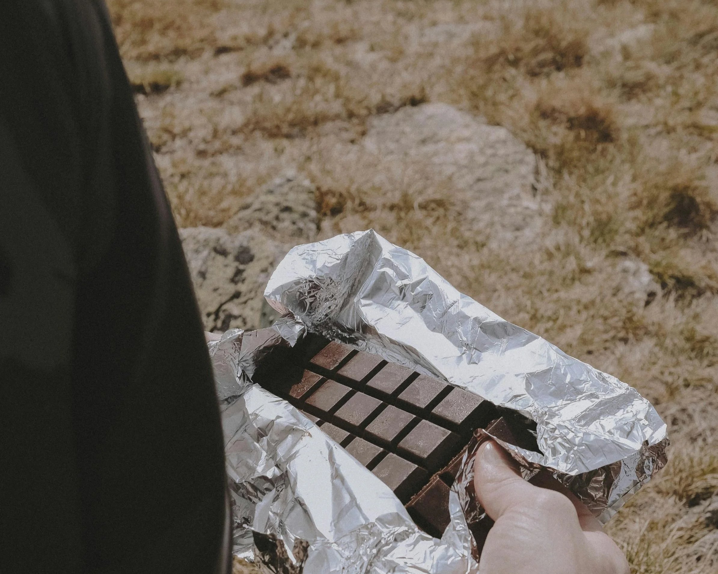 On a grassy background, a close-up of a female hand holding an open bar of chocolate.