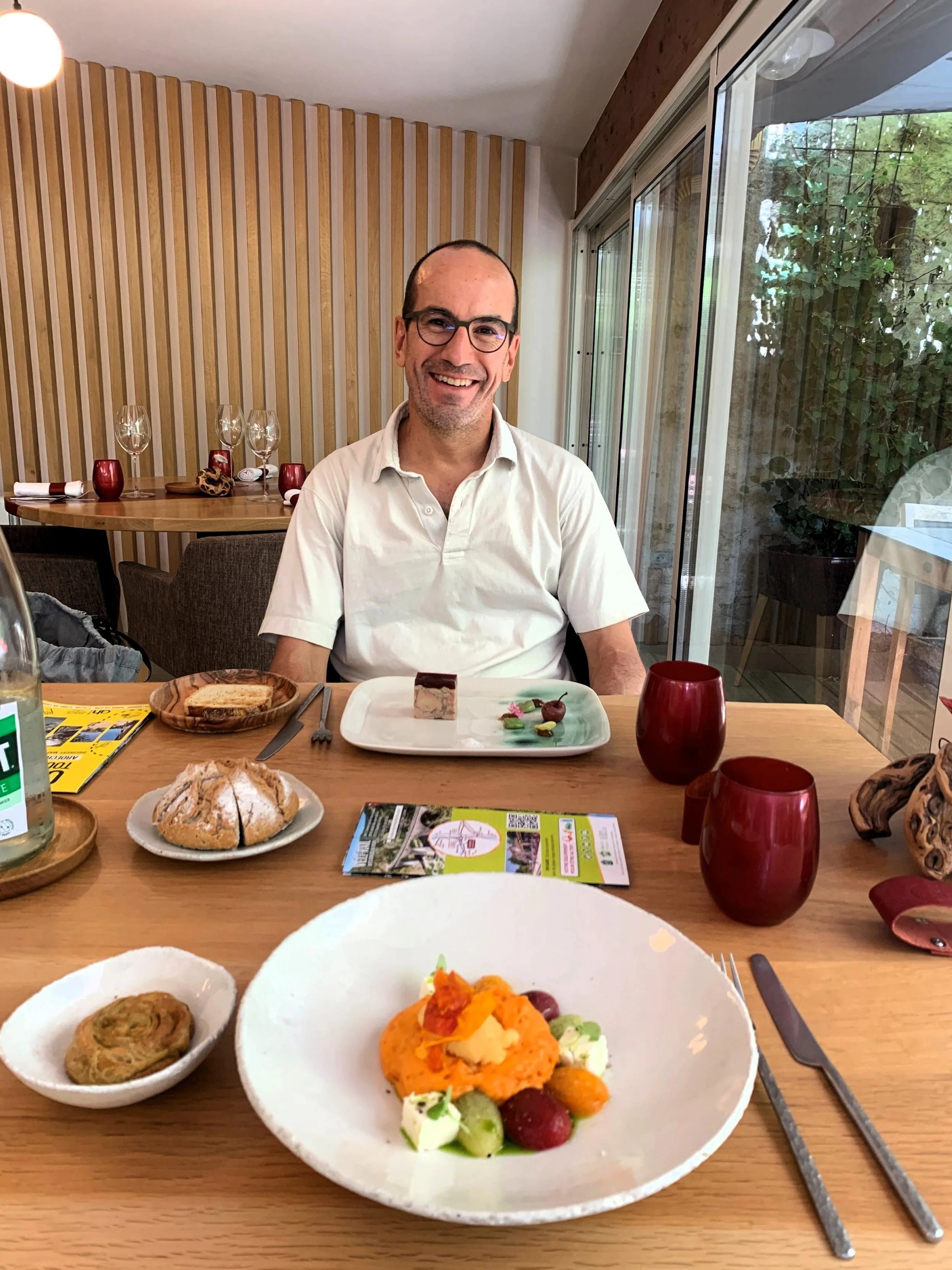 A table with plates displaying two appetizer portions accompanied by crushy bread, with a smiling man seated on the opposite side.