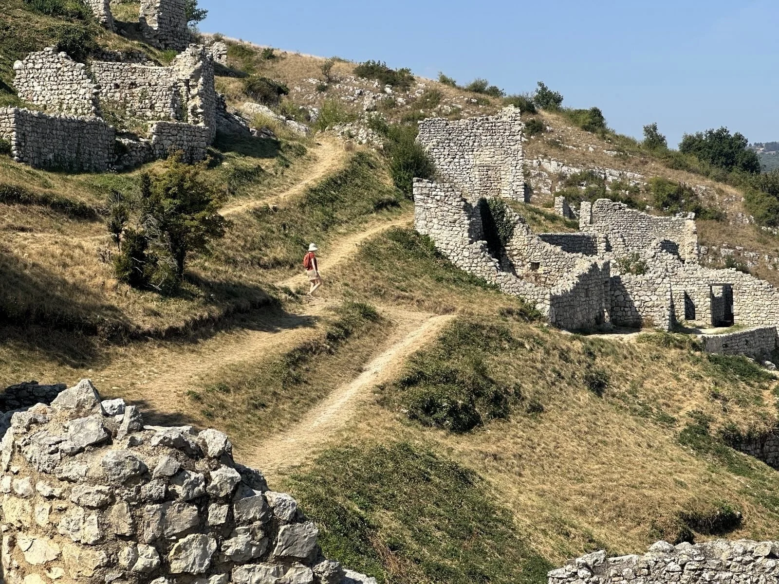 Footpaths switchbacking up a steep slope amid stone castle ruins.