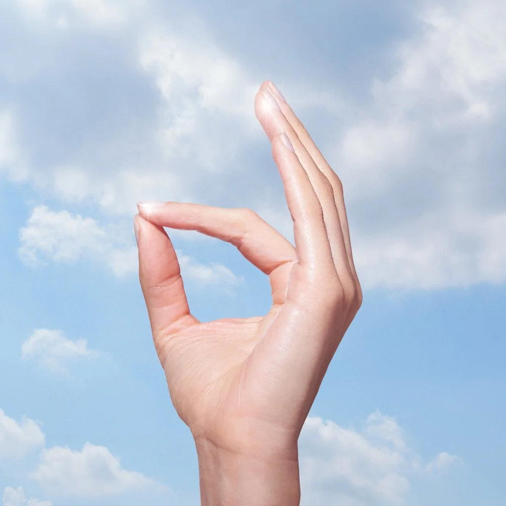 Hand in gyan mudra against a blue sky with clouds