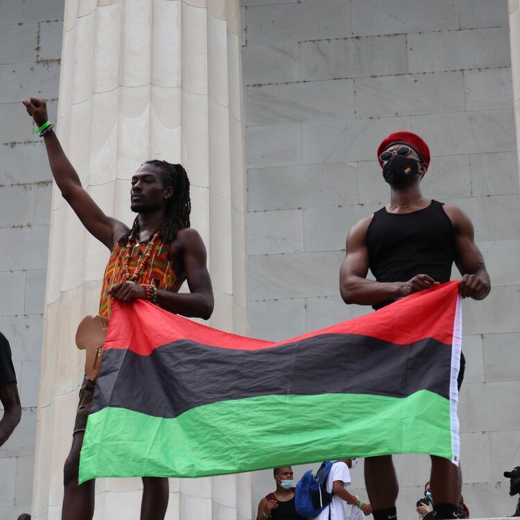 Two men hold up the pan-African flag on the edge of the Lincoln Memorial during speeches by activists and families of victims of police brutality and racism.