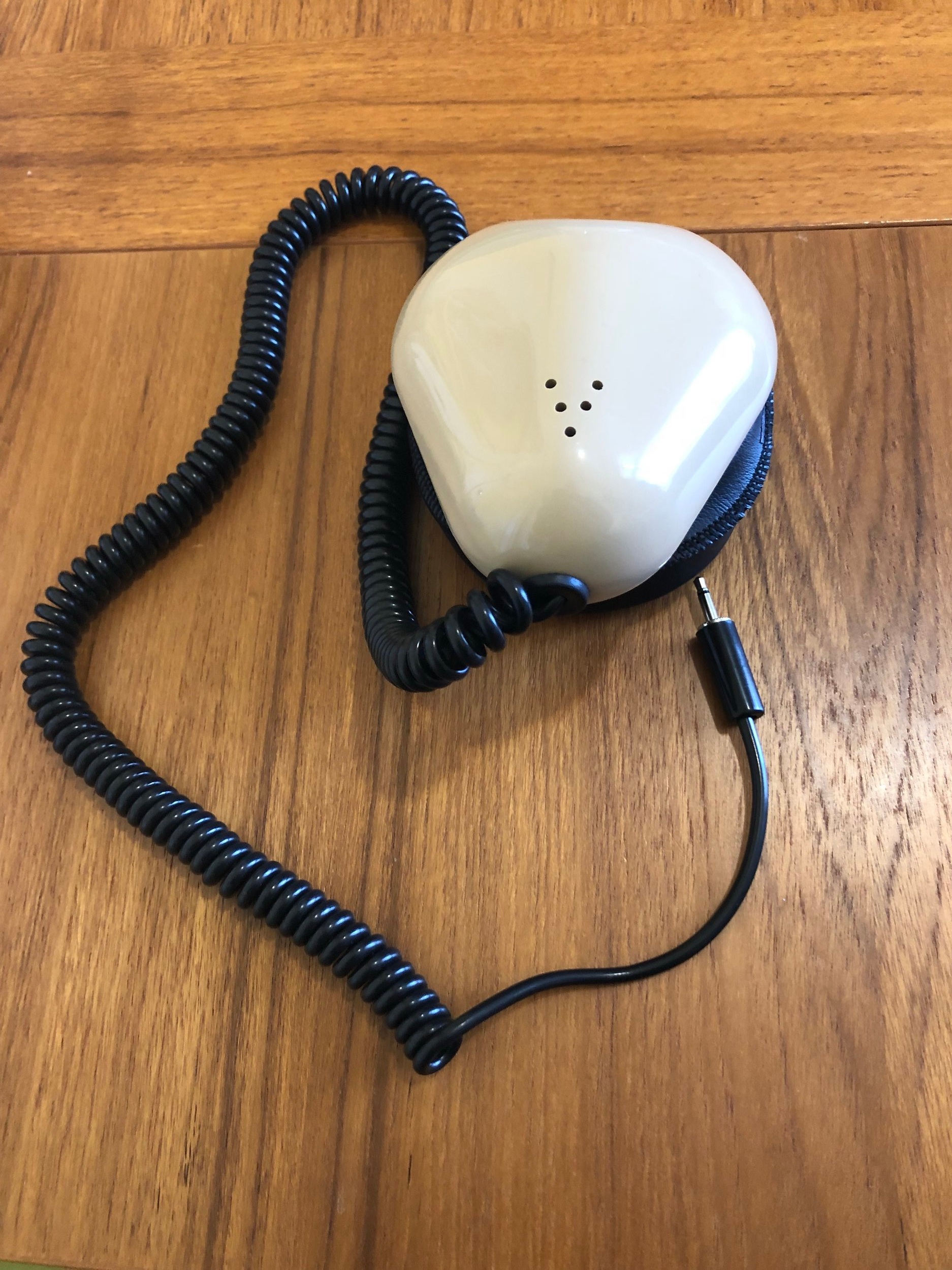 [A 'stenographer's mask' rests on a table it is a mouth sized metal case&nbsp; containing a microphone with a flexible seal that fits around the mouth. A small microphone cable is attached.]