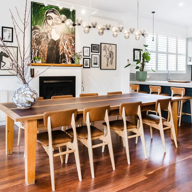 Gallery wall of art behind a large dining table with leather dining chairs