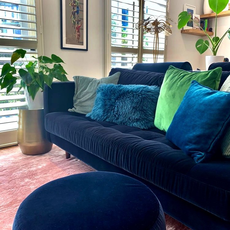 Pink rug with navy blue velvet sofa, fluffy cushions and a butterfly table lamp in a living room designed by Hue and Space Interior Design