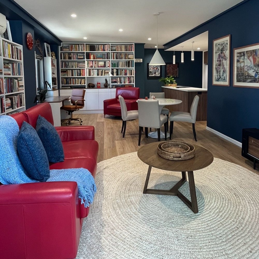 Blue walls in living room with round beige rug, timber coffee table and dining set.