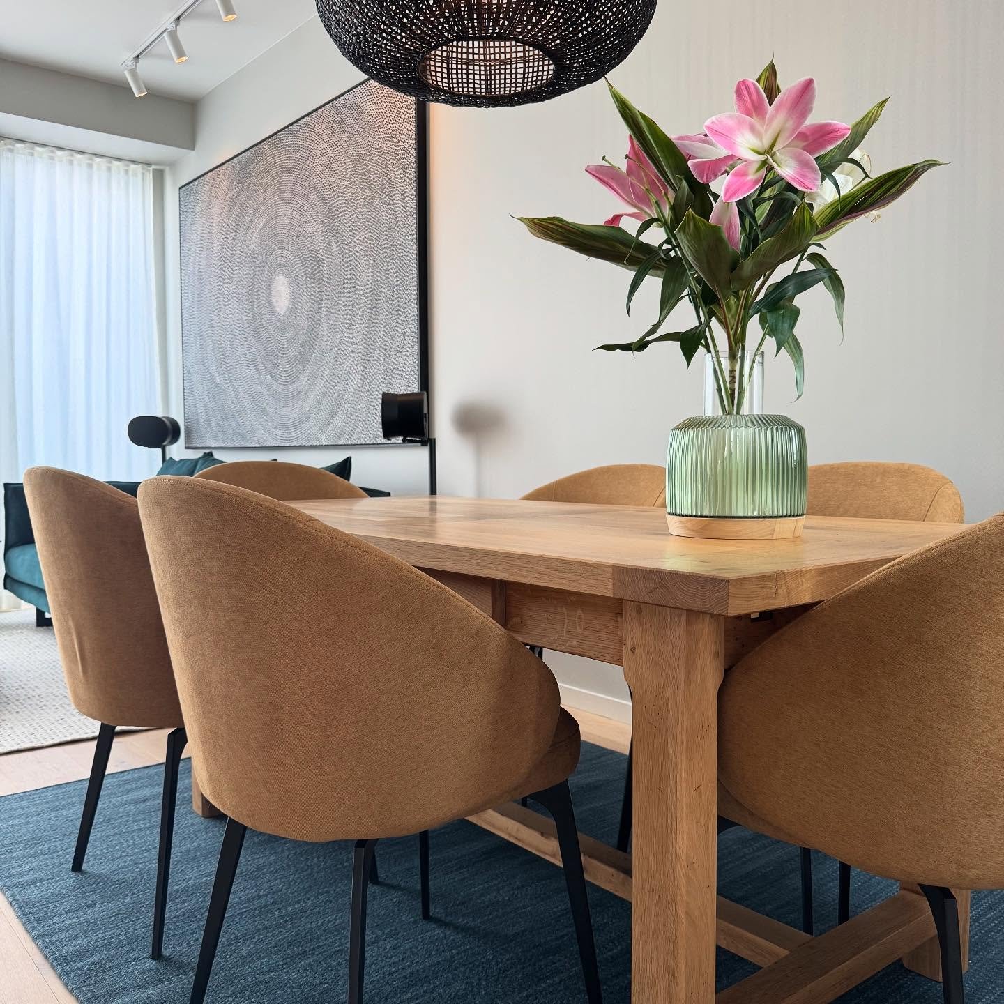 Natural tones, soft textures, and a touch of sculptural elegance. This dining area is all about balance &mdash; warm timber, earthy mustard chairs, a woven black pendant, and just the right pop of colour from fresh blooms. It&rsquo;s calm, modern, an