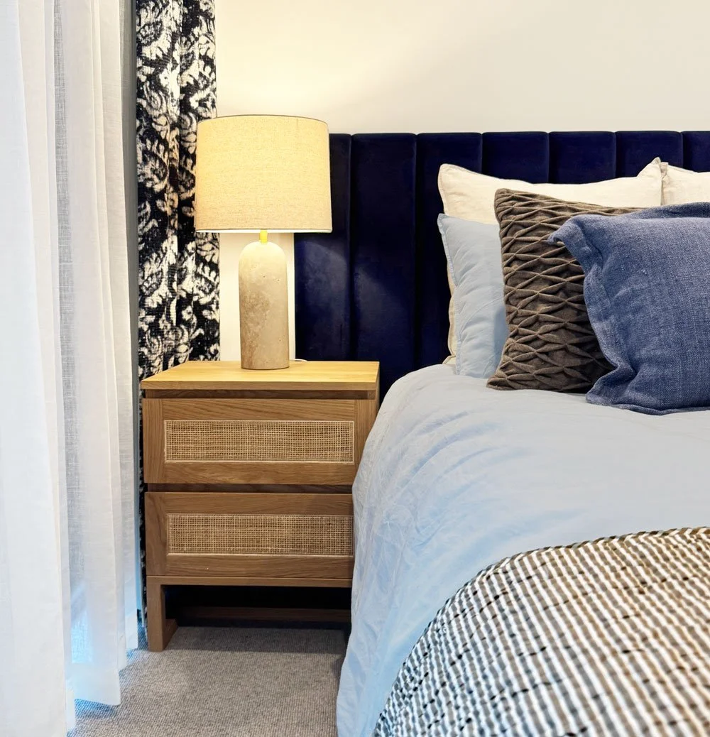 Soft light, rich textures and a palette that actually helps you switch off. 

The warm glow of that sculptural bedside lamp, paired with a velvet navy headboard, woven timber bedside tables, and layered bedding, creates a bedroom that feels calm, war
