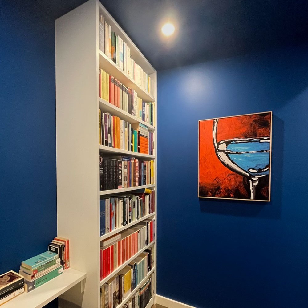 White custom bookshelf stands out against the bright blue walls and orange artwork in this home office designed by Hue and Space Interior Design