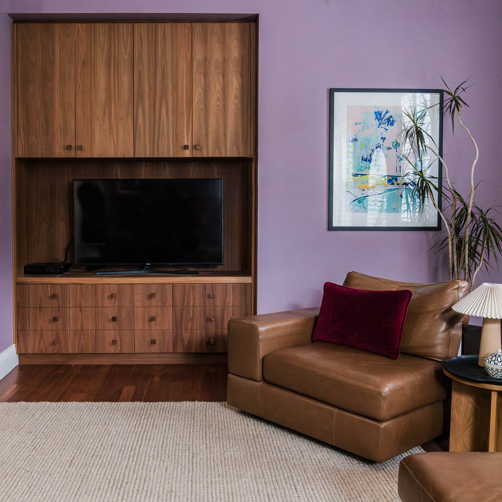 Custom joinery and a leather chair in a cosy living room with mauve walls