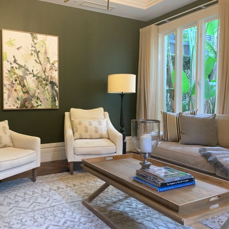 Pale neutral fabric sofa and chairs in French Provincial style, with timber coffee table and green floral art hung on olive green walls. Interior Design by Hue and Space