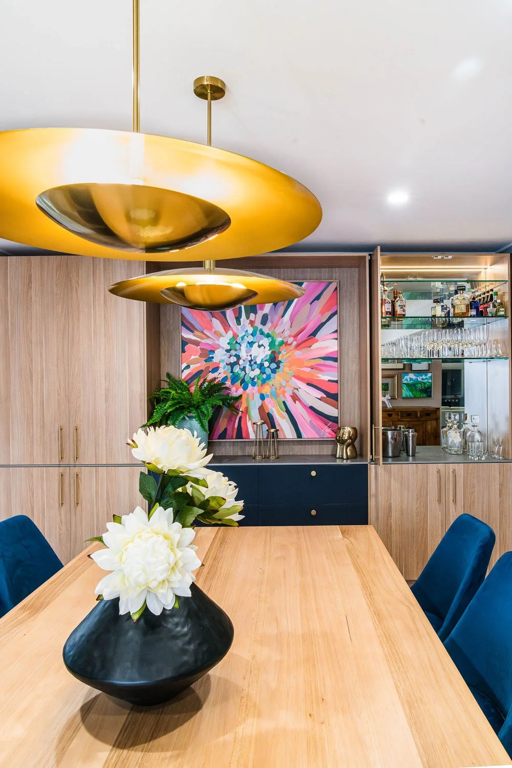 Custom Joinery with bar, timber dining table , bold brass light fixtures and joyful art in bright colours