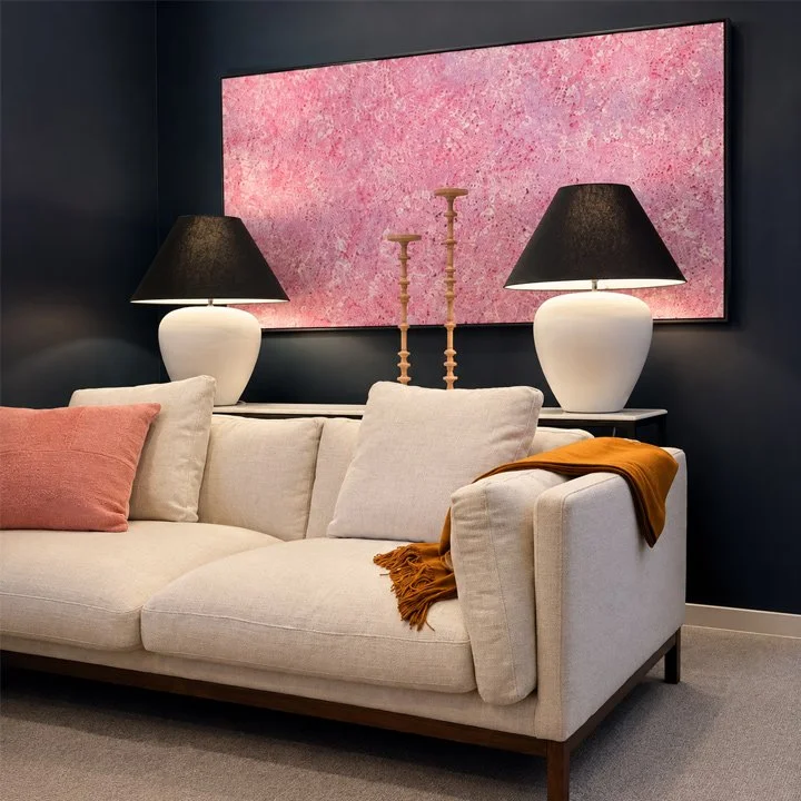 close up of bright pink indigenous art and a pale sofa with ochre and rust decor. The console behind the sofa has two large table lamps and clay candle sticks