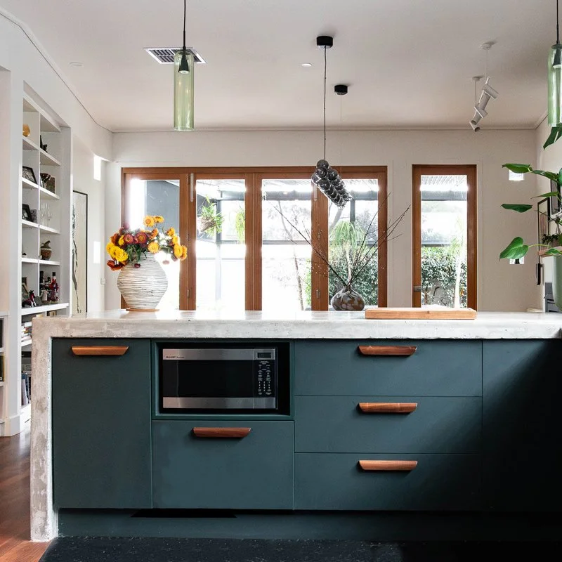 Concrete kitchen benchtop with dark green cabinets and timber handles