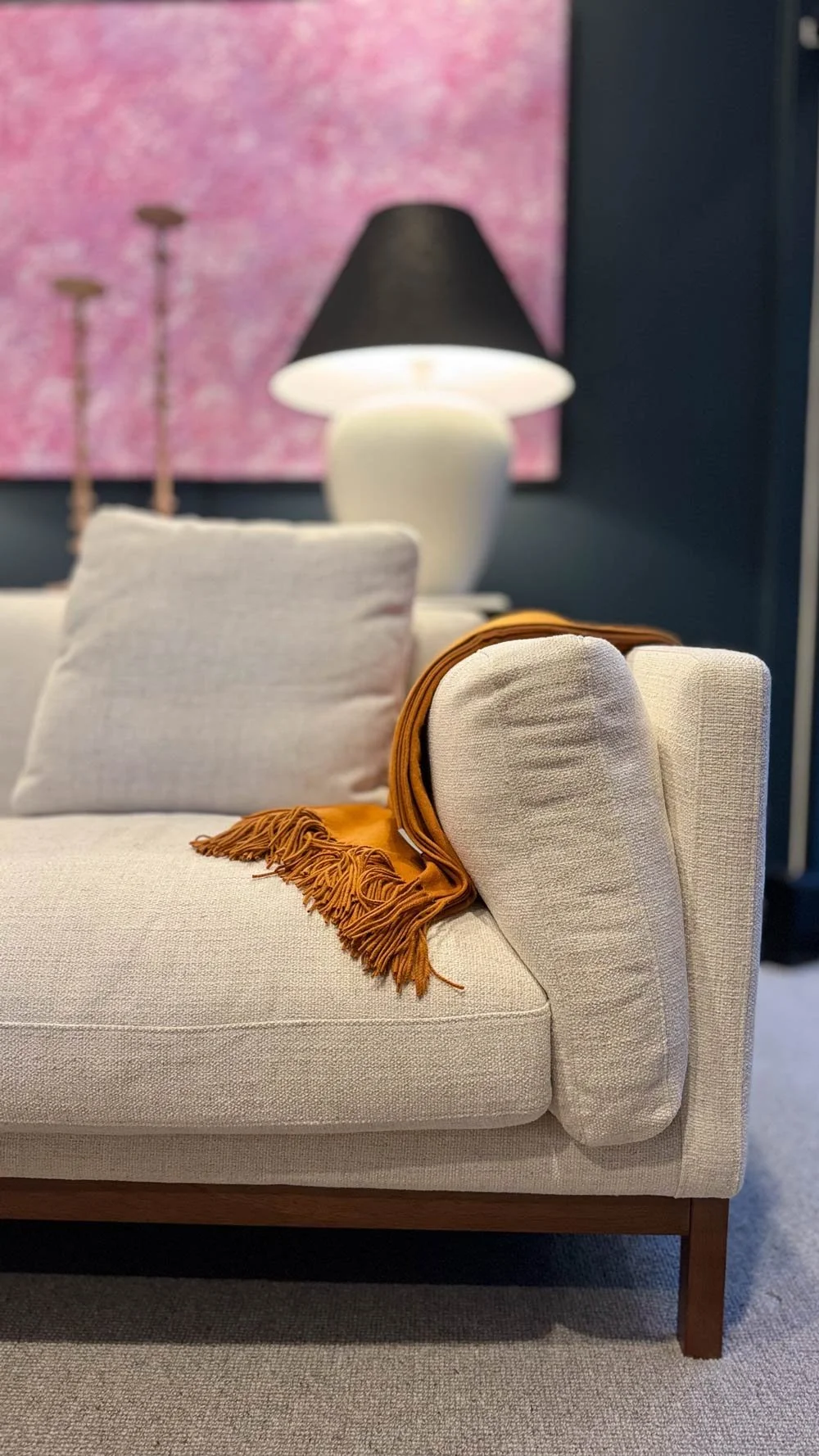 close up of sofa with ochre throw blanket and lamp candlesticks and pink indigenous art in the background