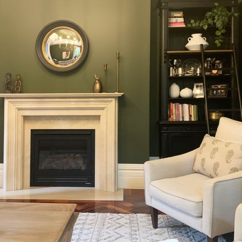 Green painted walls in formal living room with black accents in mirror and bookshelf design by Hue and Space Interiors