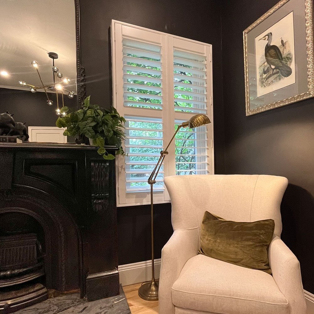 Comfortable chair by a fireplace with bird art prints and white plantation shutter desifned by Hue and Space Interior Design