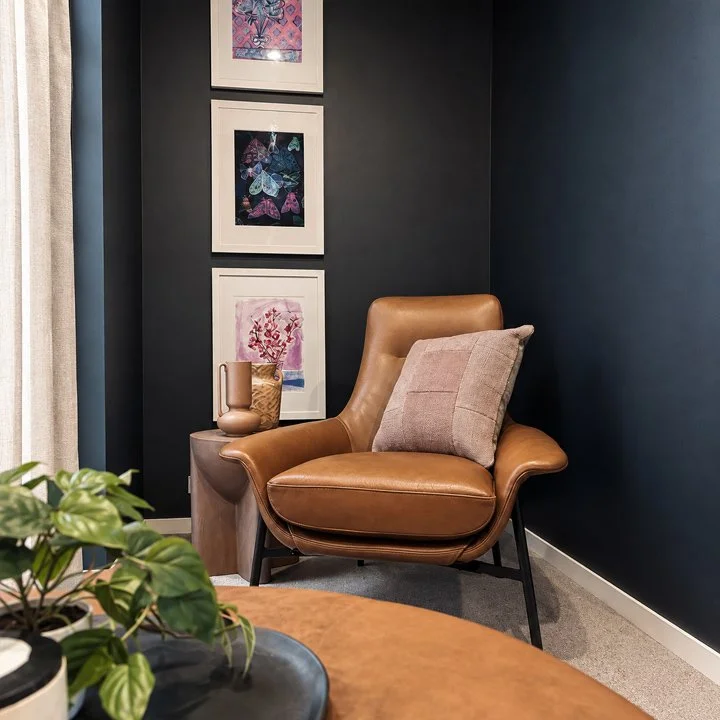 Leather chair sits in the corner of the room with three art prints hung vertically to fill the space.