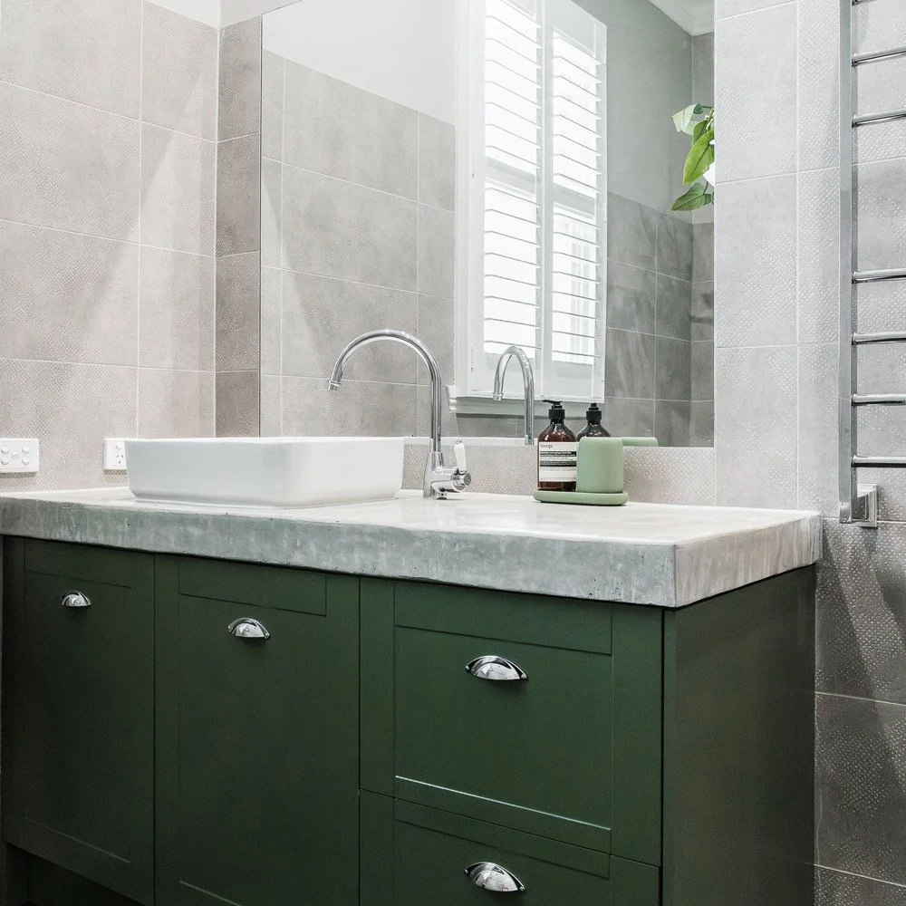 Green bathroom vanity with concrete counter top and white ceramic bowl