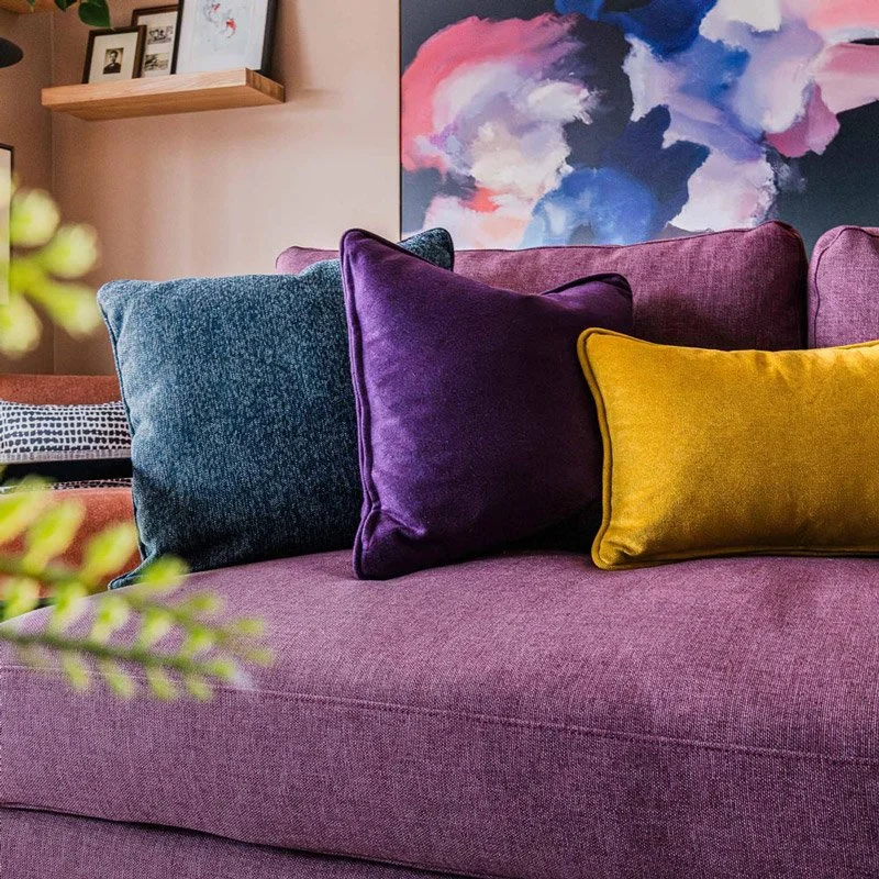 Bright purple sofa with blue and yellow cushions and colourful art behind