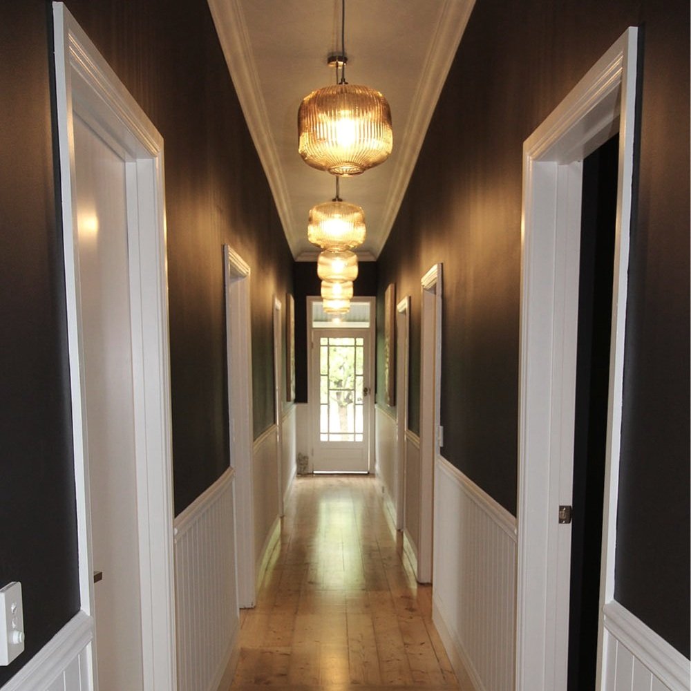 Hand blown glass pendant lights in a hallway with dark walls and white wainscoting panelling designed by Hue and Space Interior Design