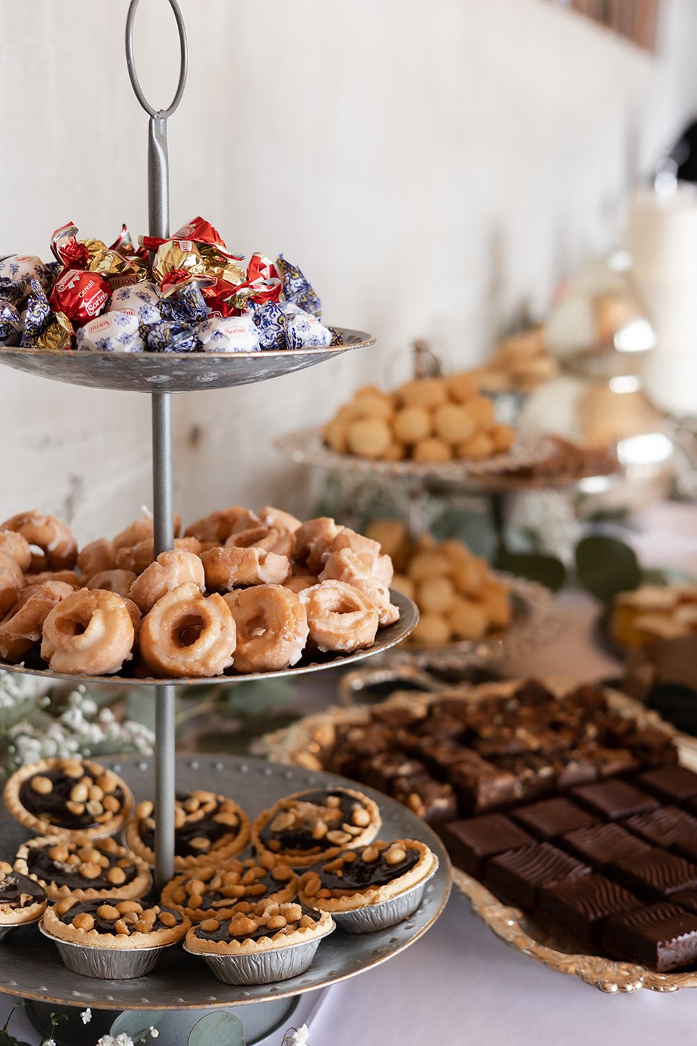 tiered wedding dessert bar display with chocolates donuts and mini chocolate hazelnut pies