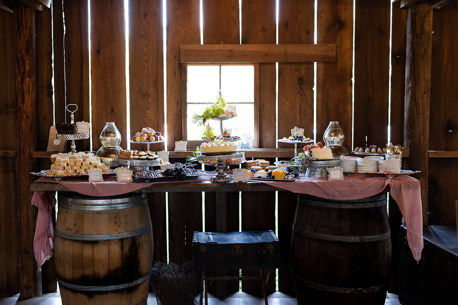 large dessert table displayed on wine barrels at barn wedding 