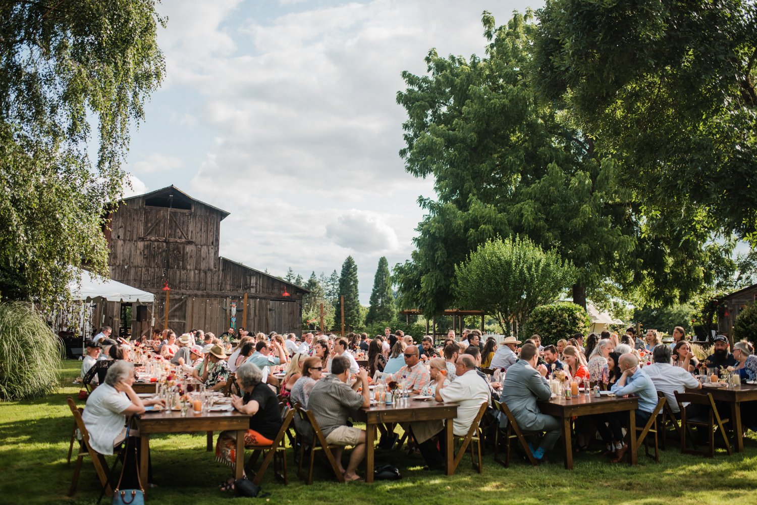 large wedding party eating dinner at rustic outdoor wedding venue in oregon