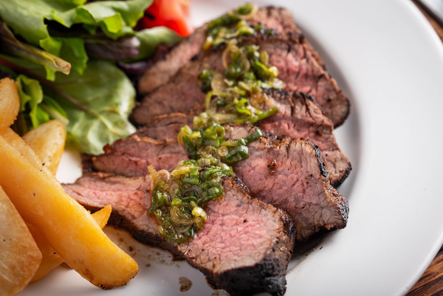 sliced steak with homemade chimichurri sauce served with greens and roasted vegetables