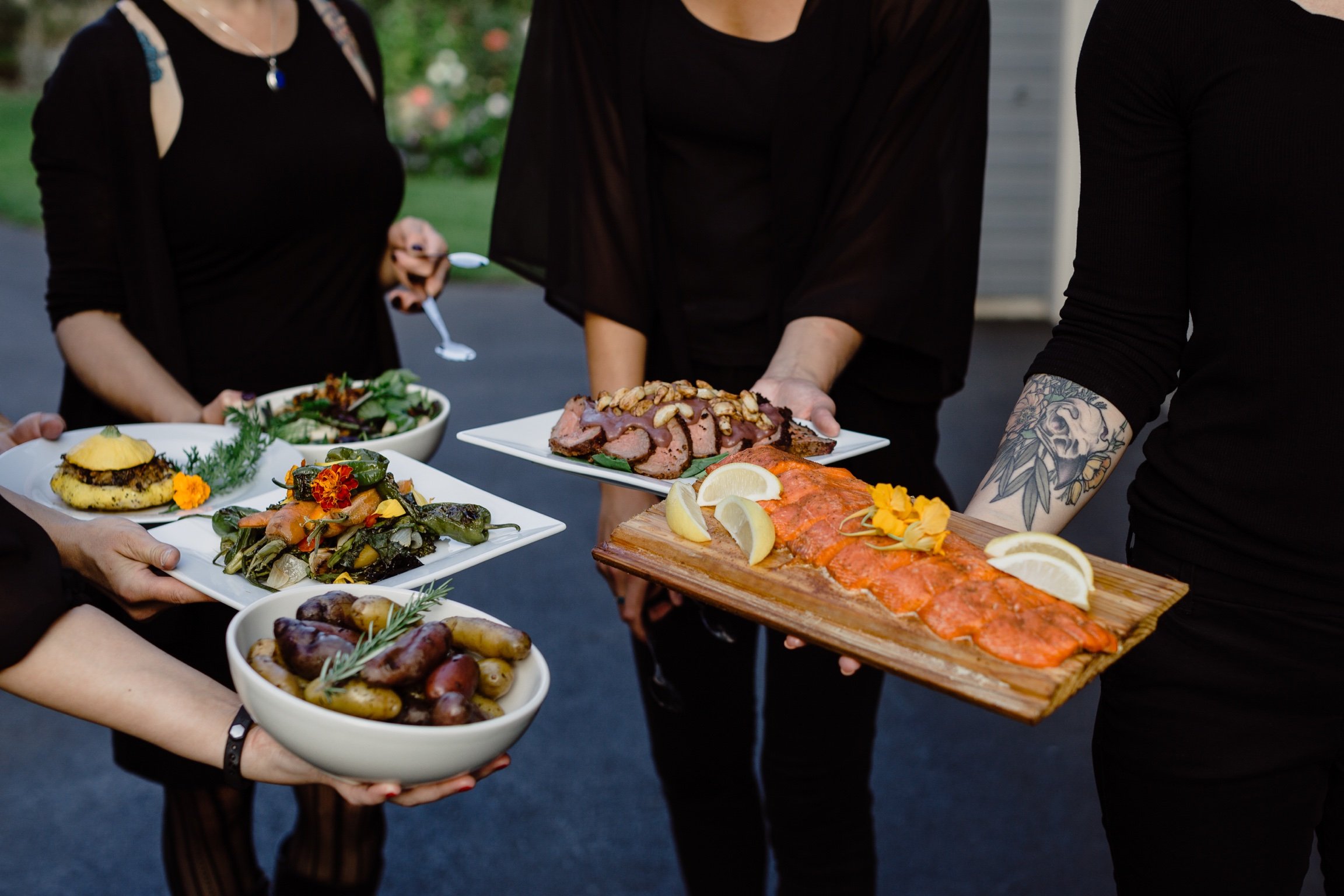 catering staff holding a variety of menu items including smoked salmon, mixed greens salad, and roasted vegetables