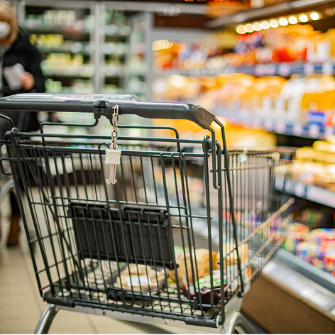 Empty shopping cart in a grocery store aisle with shelves of snacks and food items.