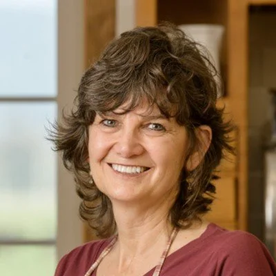 Smiling woman with short, curly brown hair in a casual indoor setting.