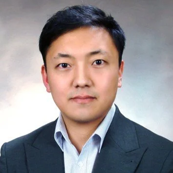 Portrait of a man in a suit and collared shirt against a neutral background.