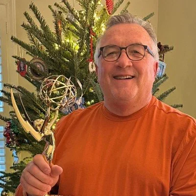 A smiling man with glasses holding a trophy in front of a decorated Christmas tree.